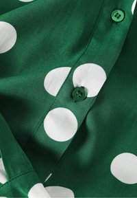Tissu vert avec de grands pois blancs et des boutons verts cousus le long d'une couture.