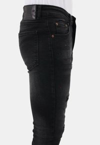 Zwarte denim jeans met een slim fit, verouderde details en een taillebandlabel met een schedelontwerp, benadrukt door koperen nit. 