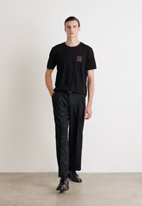 Zwarte katoenen T-shirt met rood "HUGO" logo op de borst, gecombineerd met zwarte broek en zwarte dresschoenen. Eenvoudig en strak ontwerp.