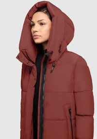 Riebi žieminė striukė sodrios raudonos spalvos su dideliu gaubtu, priekinė užtrauktuku ir juodais akcentais. Yra siuvinėtas raštas ir šoniniai kišenės funkcionalumui.