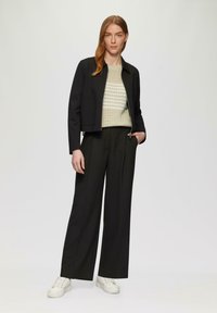 Zwarte cropped jack over een lichtgekleurde, gestructureerde trui, gecombineerd met hoge zwarte broeken en witte sneakers.