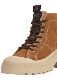 Bruine hoge sneakers met een suède textuur, contrasterende zwarte veters en een dikke, gestructureerde rubberen zool, voorzien van een logo op de tong.