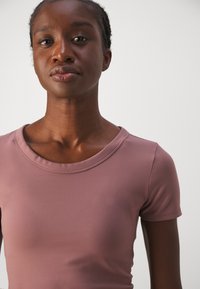 Lühikeste varrukatega, kehaümberdv top neutraalses mauve värvitoonis, valminud siledast venivast kangast. Omab ringikujulist kaelust, millel on peen õmbluse detail.