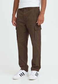 Braune Cargo-Hosen mit Seitentaschen, aus strukturiertem Stoff, im lässigen Schnitt und mit geradem Bein, kombiniert mit weißen Sneakern.