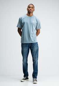 Lichtblauwe katoenen t-shirt met korte mouwen en een ronde hals, gecombineerd met donkerblauwe denim jeans en zwart met een patroon sneakers.