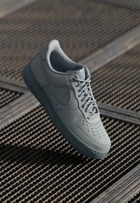 Svijetlosivi kožni tenisice s perforiranim nosom, teksturiranim srednjim dijelom, ravnim vezicama i Nike swoosh logotipom sa strane. Vidljiva gumena potplata.