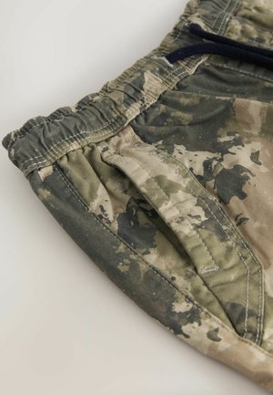 Pantaloni scurți de camuflaj cu un tiv elastic, două buzunare laterale și un material texturat care prezintă nuanțe de verde și bej.