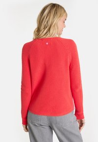 Korallenfarbener Strickpullover mit gerippter Textur, Rundhalsausschnitt und Raglanärmeln. Mit einem rosa Knopfdetail hinten und einer lockeren Passform.