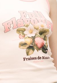 Μπλουζάκι χωρίς μανίκια με ροζ τελείωμα που φέρει το κείμενο «Full Flavour», βοτανική απεικόνιση φραουλών και λουλουδιών, και «Fraises de Nîmes France 1960».
