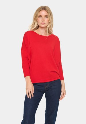 Rode, geribbelde gebreide top met een bootnek en driekwartmouwen, gecombineerd met donkere denim jeans. Eenvoudig en relaxte pasvorm.