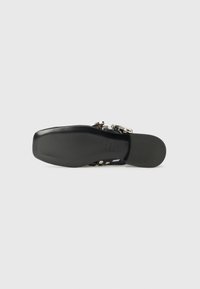 Schwarze Sandale mit einer glatten Sohle, ausgestattet mit metallischen Riemen und Akzenten, die ein elegantes, minimalistisches Design präsentieren.