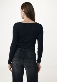 Maglia a maniche lunghe nera a coste abbinata a jeans grigi scuri a vita alta, con tasche posteriori e leggere scoloriture. Design semplice e aderente.