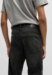 Jeans de mezclilla negros con un corte ajustado, ligera desgastación y bolsillos traseros con costuras reforzadas. Camiseta gris con cuello redondo.