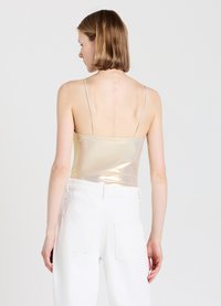 Top fitted metallico dorato con spalline sottili, abbinato a pantaloni bianchi a vita alta. Texture liscia e design minimalista.