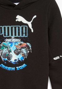 Sudadera negra con logo blanco de Puma, camiones monstruo coloridos chocando, y texto azul que dice "Zona de Choque Power Smashers" en el frente.
