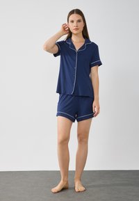 Marinblå pyjamas set med kort ärm och shorts, med vit piping längs kragen och ärmsluten. Mjuk, lättviktig tyg.