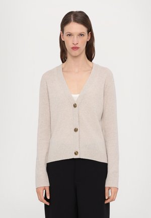 Beige strikket cardigan med V-hals, lange ermer og fem store brune knapper foran. Ribbestrikkede mansjetter og nederkant gir tekstur.