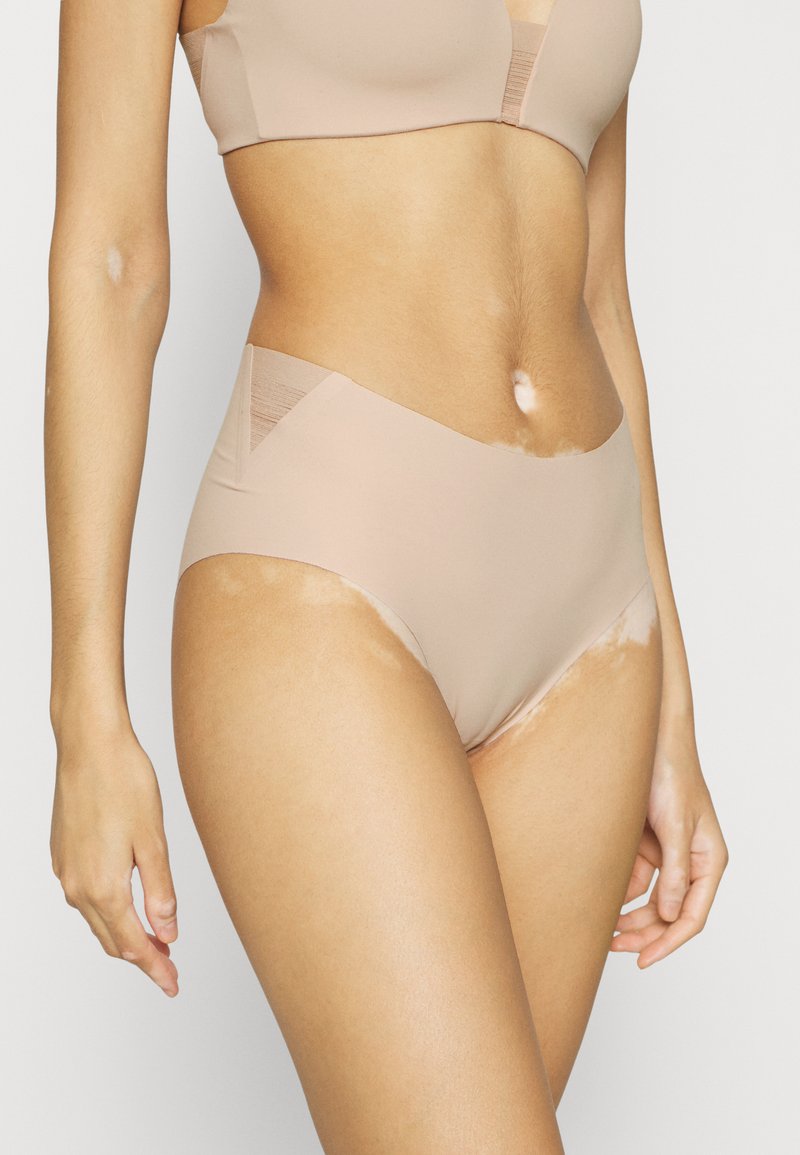 Beige hooggezette onderbroek met een gladde textuur, zijpanelen van mesh en minimale stiksels voor een naadloze uitstraling.