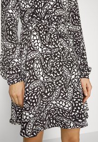Vestido preto e branco com padrão que apresenta um desenho espiralado, mangas longas, cintura com laço e bainha ampla, feito de tecido leve.