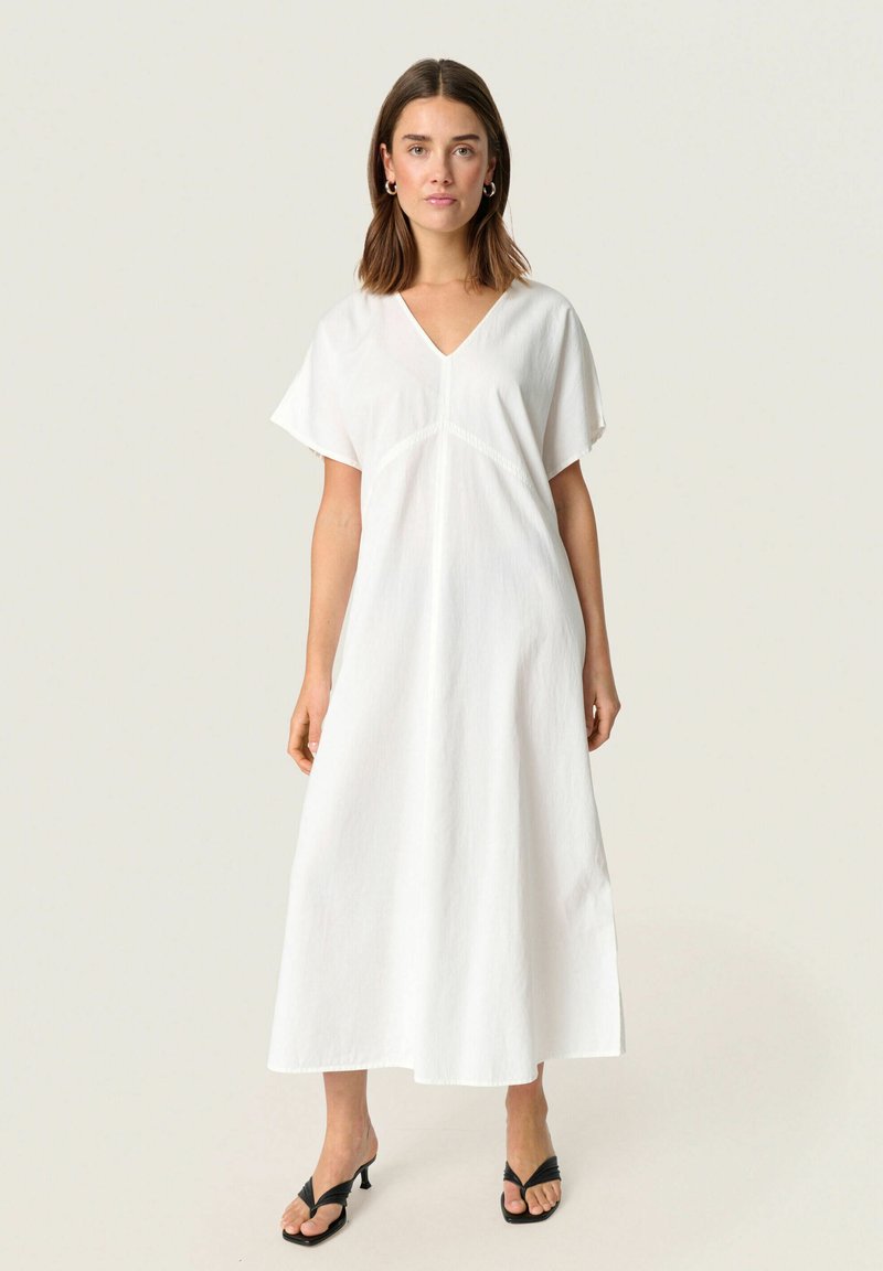 Robe blanche, jusqu'aux genoux, avec un col en V et des manches courtes. Fabriquée en tissu léger avec une finition texturée et un corsage ajusté.
