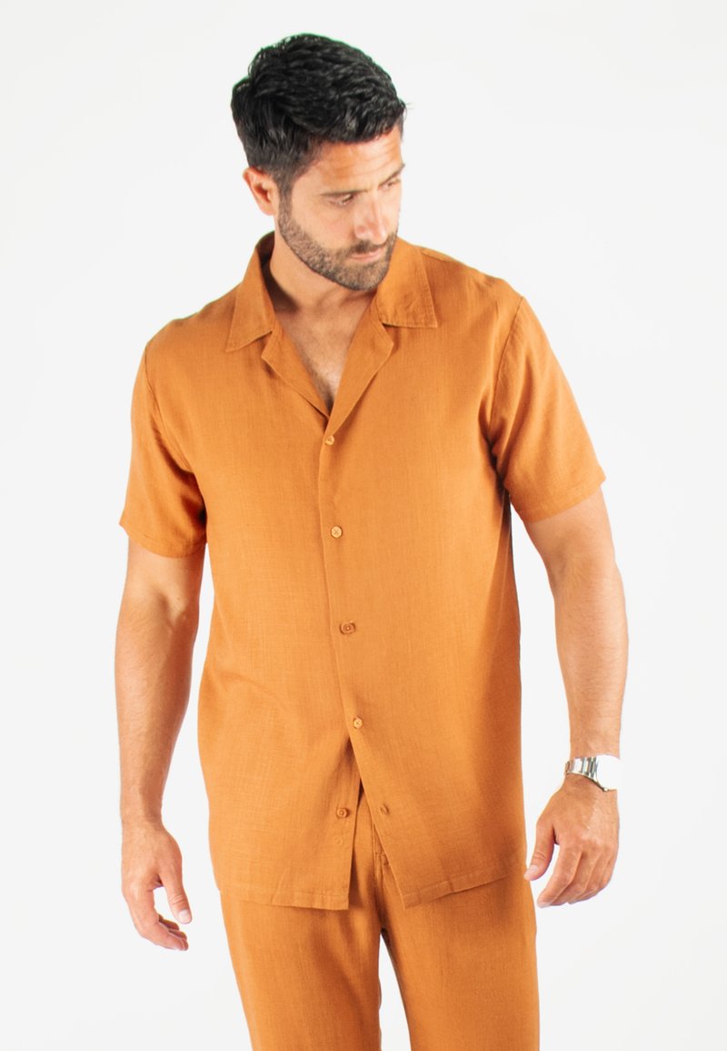 Chemise à manches courtes, col, de couleur orange brûlé, fabriquée en matériau léger avec une texture et cinq boutons sur le devant.