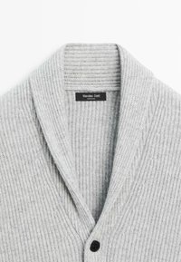 Grå ribbad kofta med sjalkrage, som har texturerad tyg, en ensam svart knappstängning och en varumärkesetikett synlig innanför kragen.