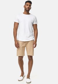 Camiseta blanca de manga corta, pantalones cortos beige con un diseño geométrico y alpargatas blancas. Conjunto casual de verano.