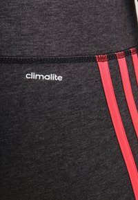 Leggings de sport noirs avec des rayures rouges sur les côtés, fabriqués dans un tissu texturé. Dotés d'un logo "climalite" blanc sur la ceinture.
