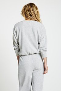 Sweat-shirt gris à coupe ample, col rond et manches longues, assorti à un pantalon taille haute de la même matière, avec une texture douce.