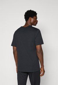 T-shirt noir à manches courtes avec un design en V. Fabriqué en coton, il a une texture lisse et une coupe décontractée, sans motifs ni embellissements visibles.