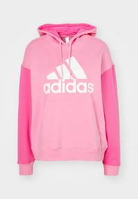 Rosa huvtröja med en vit Adidas-logotyp. Har en känguruficka och färgblockerade ärmar i varierande nyanser av rosa.