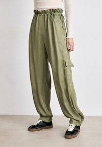 Olive green cargo pants with a gathered elastic waistband, side pockets, and a loose fit, made from smooth, lightweight fabric.