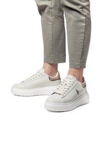 Białe skórzane sneakersy o gładkim wykończeniu, z sznurowanym zapięciem, podwyższoną białą podeszwą i subtelnym metalicznym akcentem z tyłu. Wyszywany detal z logo.