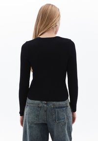 Maglietta nera a maniche lunghe con taglio aderente, abbinata a jeans blu a vita alta con tasche a contrasto e vestibilità rilassata.