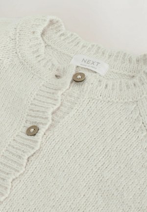 Hellbeige gestrickte Strickjacke mit einem strukturierten Muster, geripptem Kragen und fünf runden braunen Knöpfen. Das Etikett lautet "NEXT, hergestellt in Indien."
