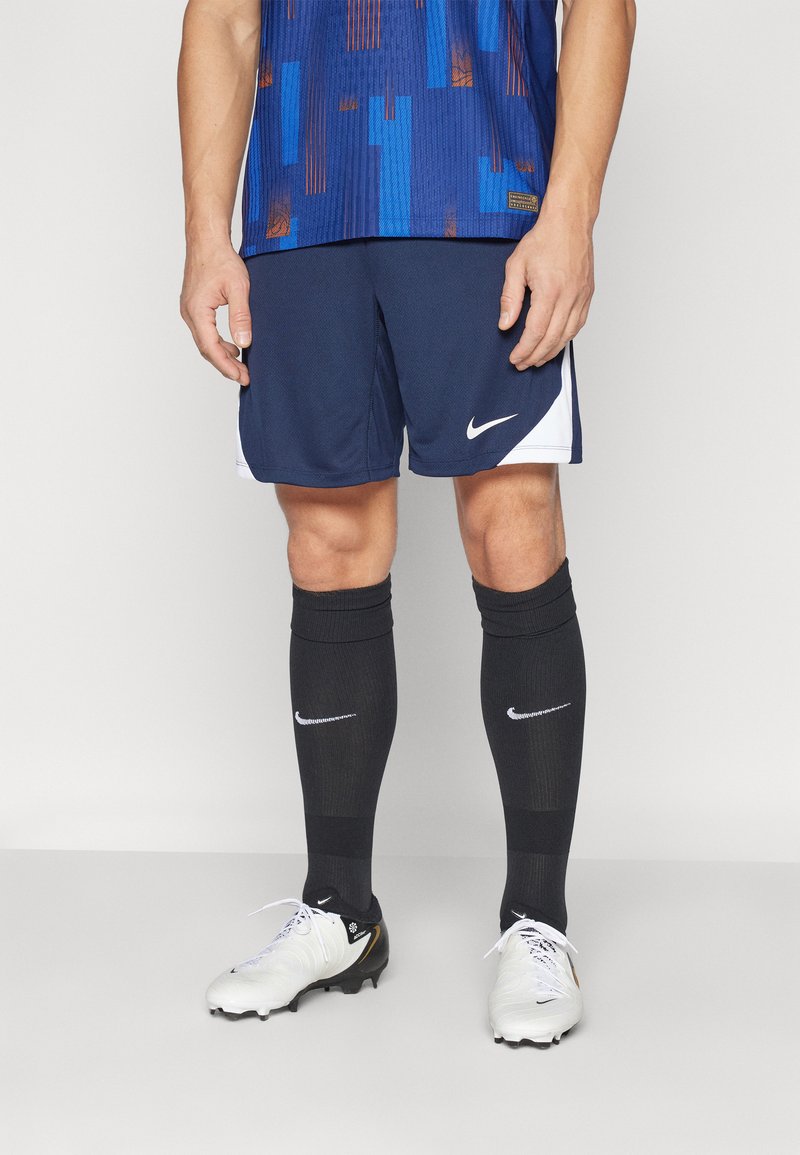 Mørkeblå Nike shorts med hvide accenter, parret med sorte knæstrømper og hvide fodboldstøvler. Har et åndbart materiale og en atletisk pasform.