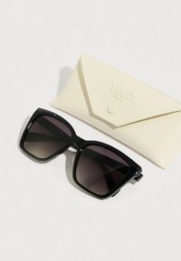 Czarne, oversize okulary przeciwsłoneczne z gradientowymi soczewkami, wraz z kremowym, teksturowanym etui z zatrzaskiem i tłoczonym logo.