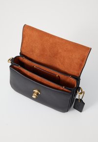Schwarze Lederhandtasche mit einem Verschluss aus goldfarbener Hardware. Das Innere zeichnet sich durch ein weiches Futter aus orangefarbigem Wildleder und zwei Fächer zur Organisation aus.