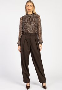Transparante blouse met lange mouwen en een bruine luipaardprint; gecombineerd met hoge, donkerbruine geruite broeken en puntige bruine hakken.