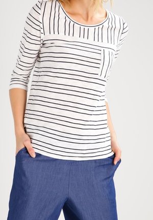 Langarmshirt mit weißen und marineblauen Streifen, mit rundem Ausschnitt und einer Brusttasche, kombiniert mit blauen Hosen.