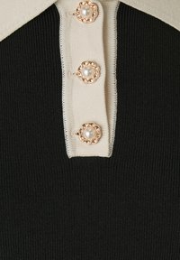 Czarny prążkowany sweter z kontrastującym kołnierzem w kolorze kości słoniowej oraz dekoracyjnymi złotymi guzikami z perłowymi środkami.