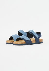 Blå mockaskandaler med korkfotbed, som har justerbara remmar och en texturerad gummisula för bra grepp. Minimalistisk design.