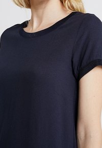 Navy modrý top s krátkým rukávem, který má zaoblený výřez a texturované akcenty na rukávech. Měkký materiál s hladkým povrchem.