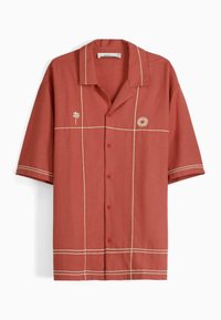 Camicia a maniche corte in ruggine con cuciture color crema. Presenta un ricamo di palma e sole. Collo classico, quattro bottoni, forma quadrata.