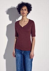 Bordowy dopasowany top z dekoltem w serek i krótkimi rękawami, w połączeniu z jasnoniebieskimi luźnymi dżinsami. Gładka faktura, minimalne detale.