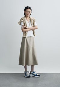 Beige leren midirok, wit geribd topje en gebreide beige sjaal. Blauw-witte sneakers zorgen voor een sportieve touch. Simpele en moderne styling.