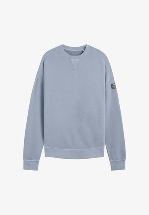Sudadera azul clara con cuello redondo, puños y dobladillo acanalados, y un pequeño detalle de etiqueta negra en la manga izquierda. Textura de tela suave.