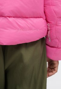 Chaqueta rosa acolchada que presenta los logos "THERMA-FIT" y "Primaloft". Acabado suave con secciones acolchadas. Combinada con tela verde olivo.