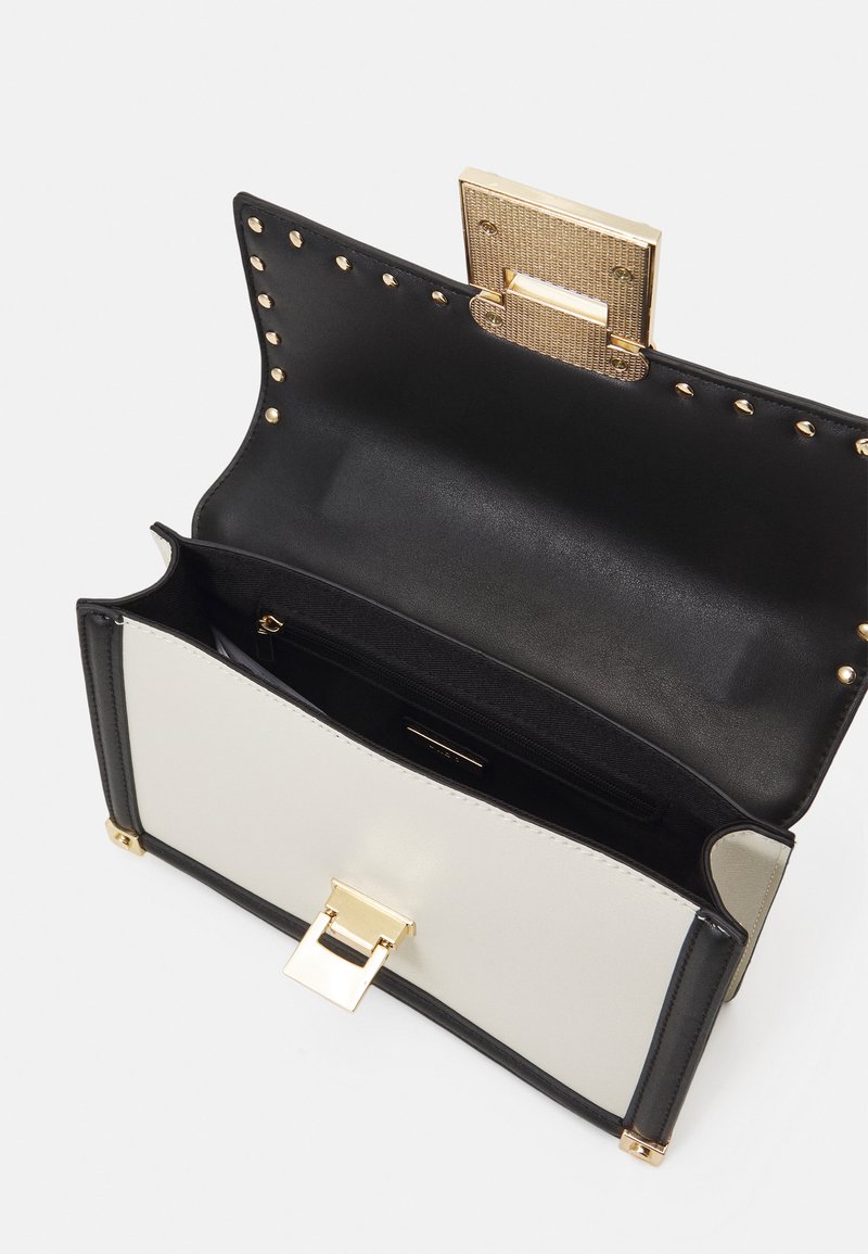 Sac à main noir et crème avec une finition brillante, fermoir en métal doré, poche intérieure et accents cloutés sur le bord supérieur.
