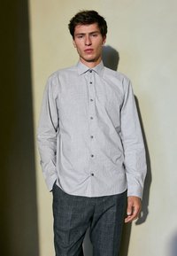 Gray button-up shirt with a subtle check pattern, long sleeves, and a pointed collar, paired with dark gray plaid trousers.